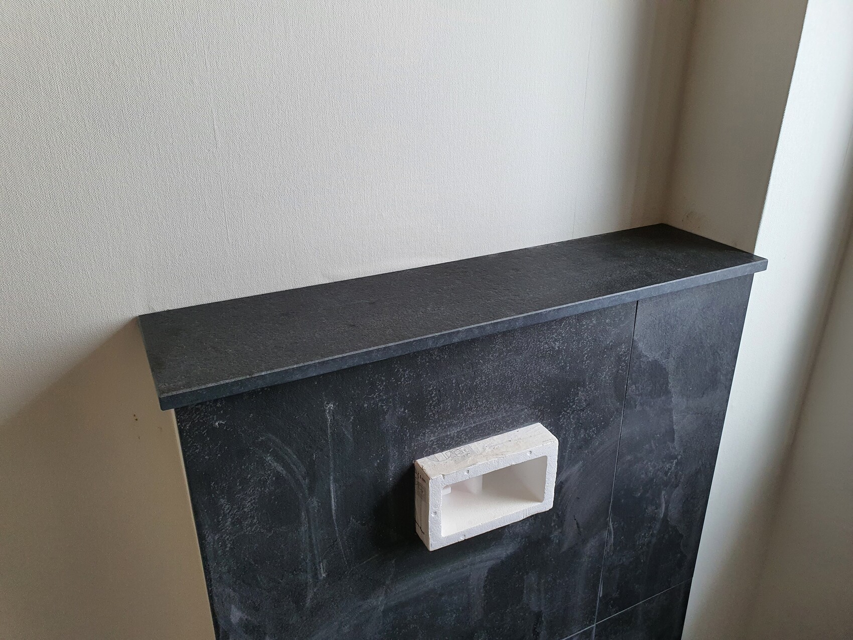 Black stone fireplace cladding with a white rectangular hollow block in the center.