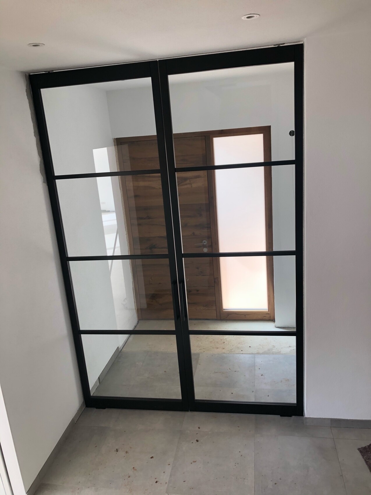 Large glass partition with black metal frame and crossbars in the hallway; wooden door behind.