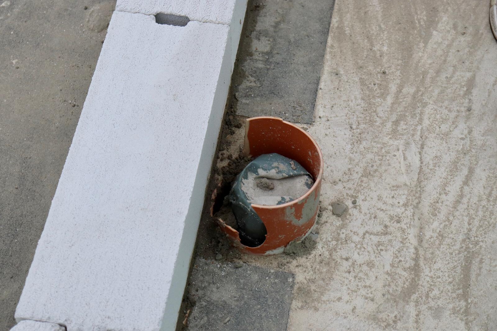 Red concrete form tube lying next to gray polystyrene block at construction site, dusty