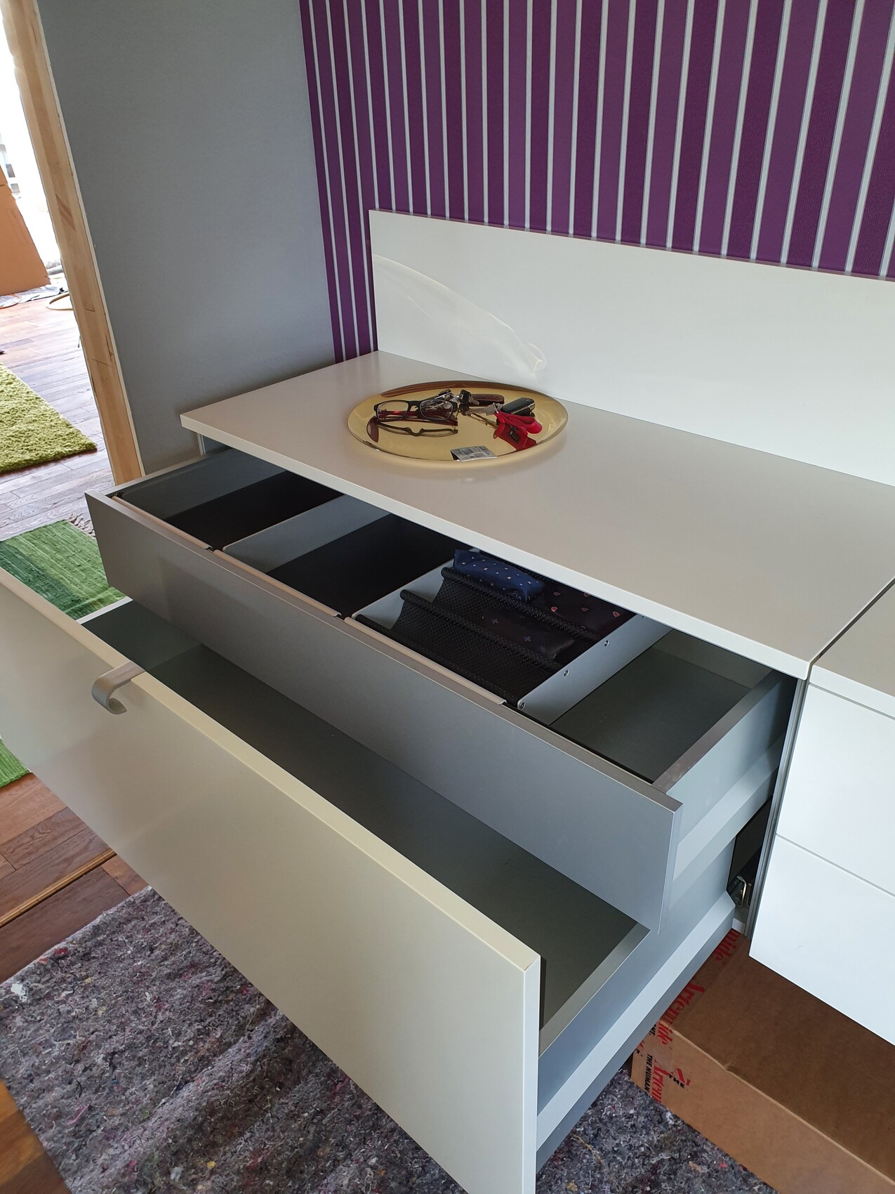 White dresser with two open drawers; top with plate, glasses, and keys, purple wall.