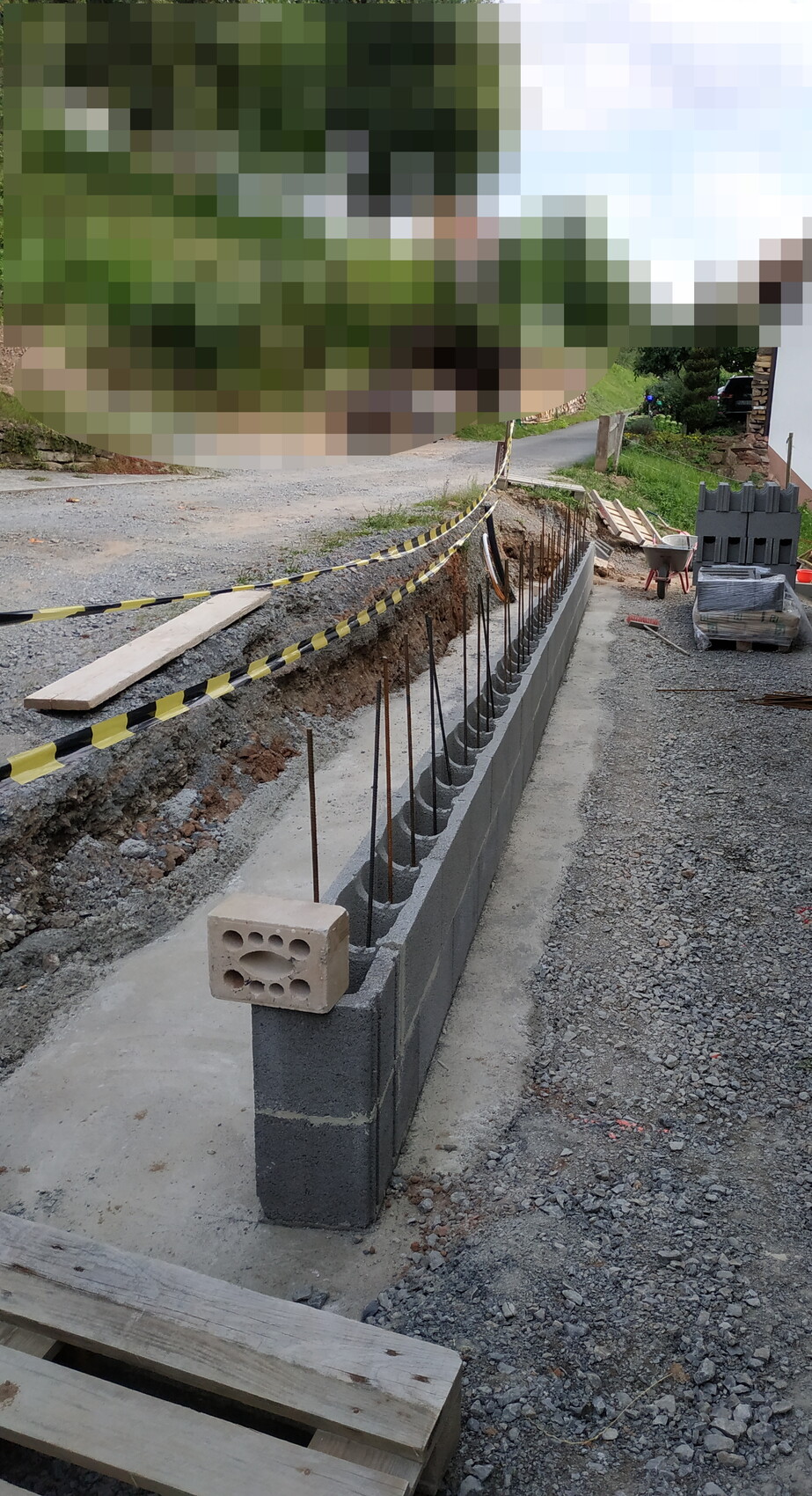 Baugrube neben Straße: Betonblockwand mit Bewehrung, Bauwerkzeuge und Material.