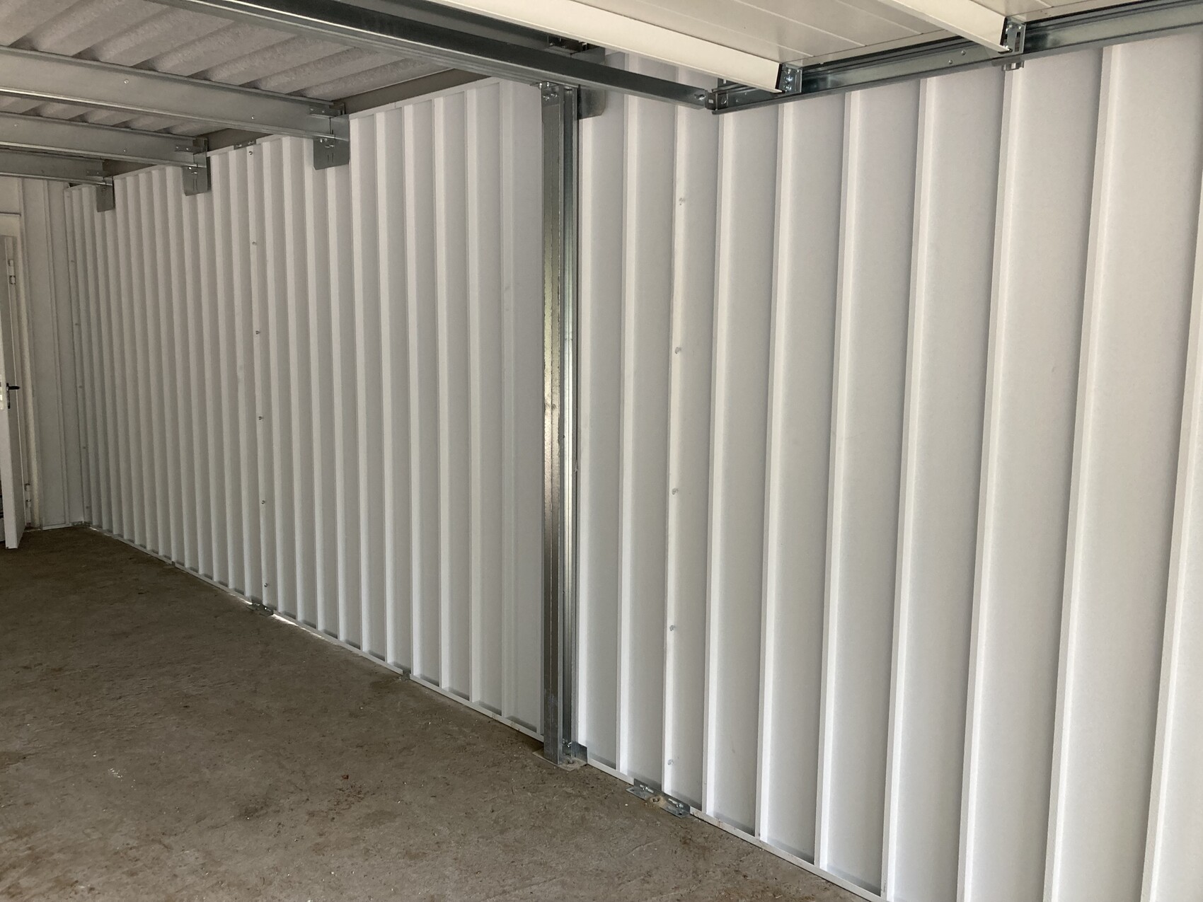 Innenraum eines Lagercontainers: weiße, gerippte Metallwände und Betonboden in einer langen Halle.