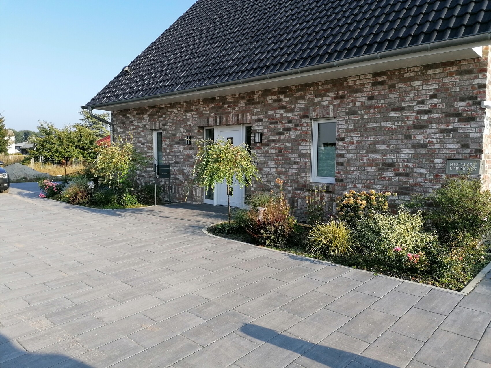 Brick house, dark roof, paved driveway and planted front garden.