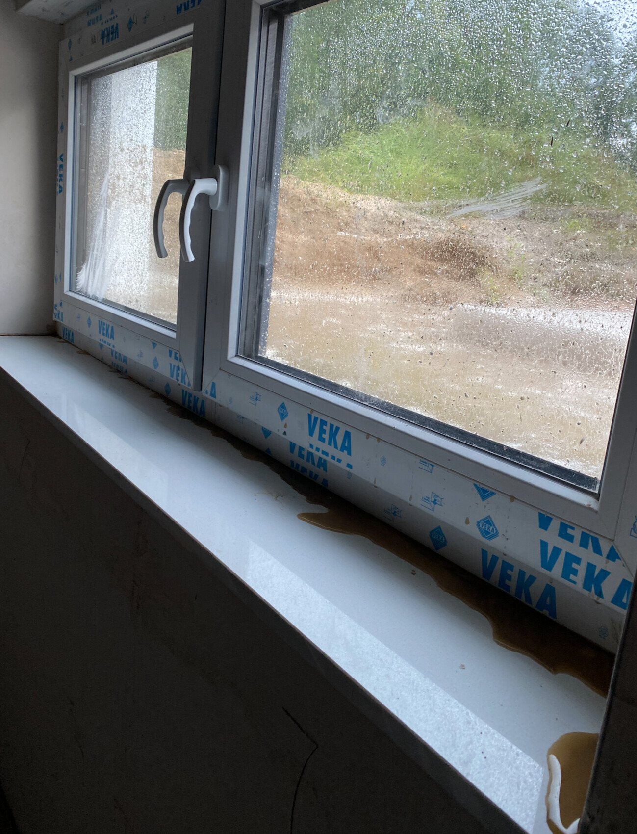 Double window under construction with VEKA film; brown liquid on the windowsill, view outside.