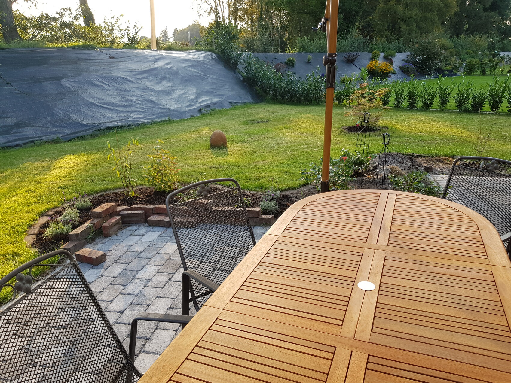 Garden: Large wooden table with metal chairs on terrace; green lawn and beds in the background