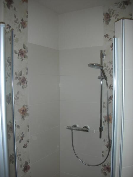 Shower enclosure with handheld showerhead, adjustable holder, glass shower screen, light tiles.