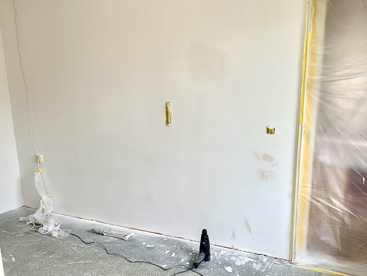White interior wall in the renovation area with socket, construction dust, and protective foil