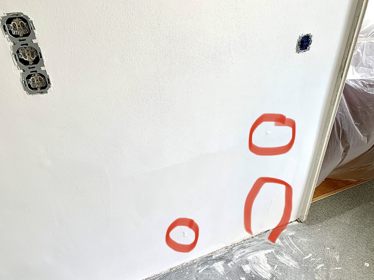 White wall with open electrical boxes on the left and three red markings on the wall.