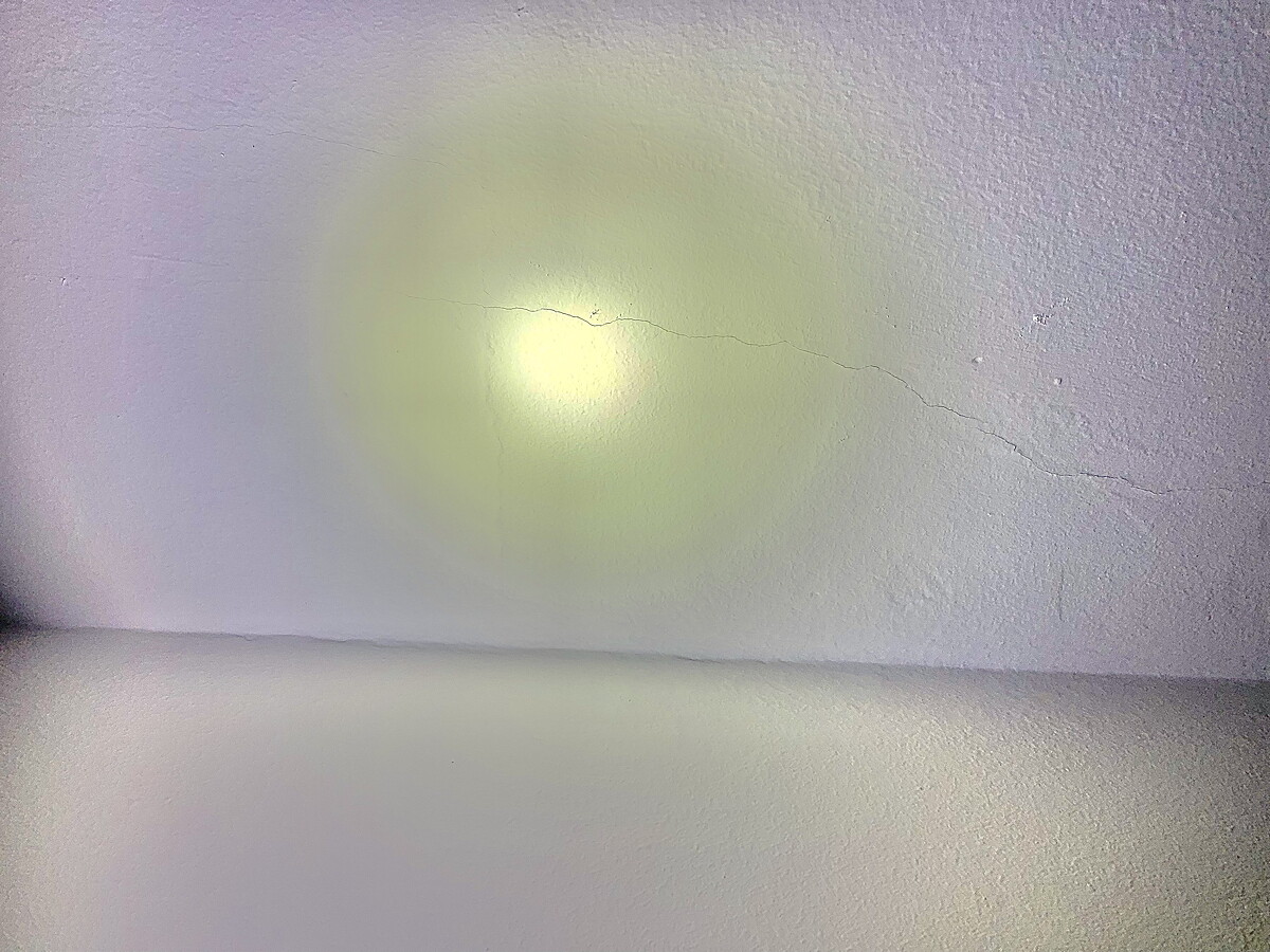 White wall with yellowish light halo, visible hairline crack, and floor at the bottom.