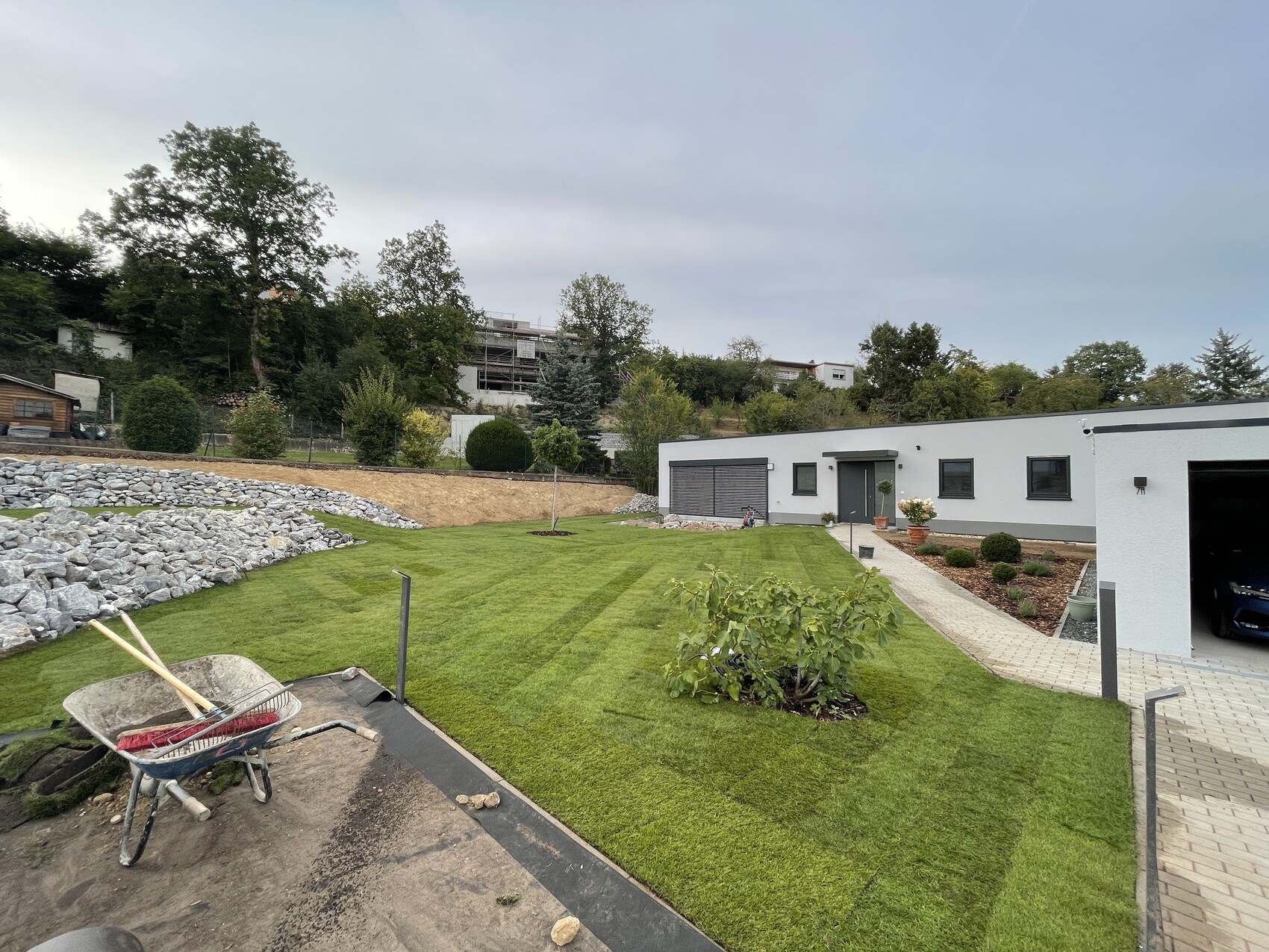 Modern single-family home with garage, well-kept lawn, walkway, and stone wall in the background.