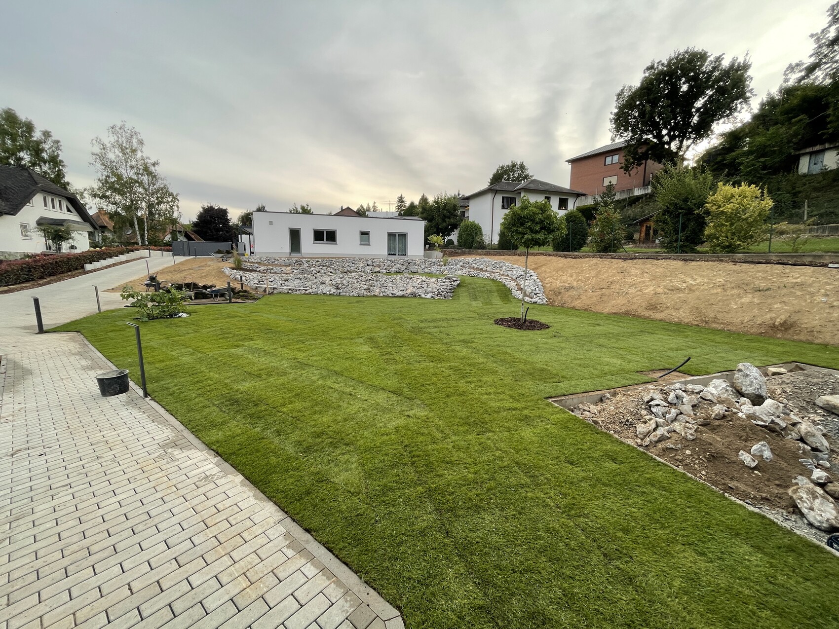 Well-maintained garden with a modern white house, stone-wall terraces, and construction work
