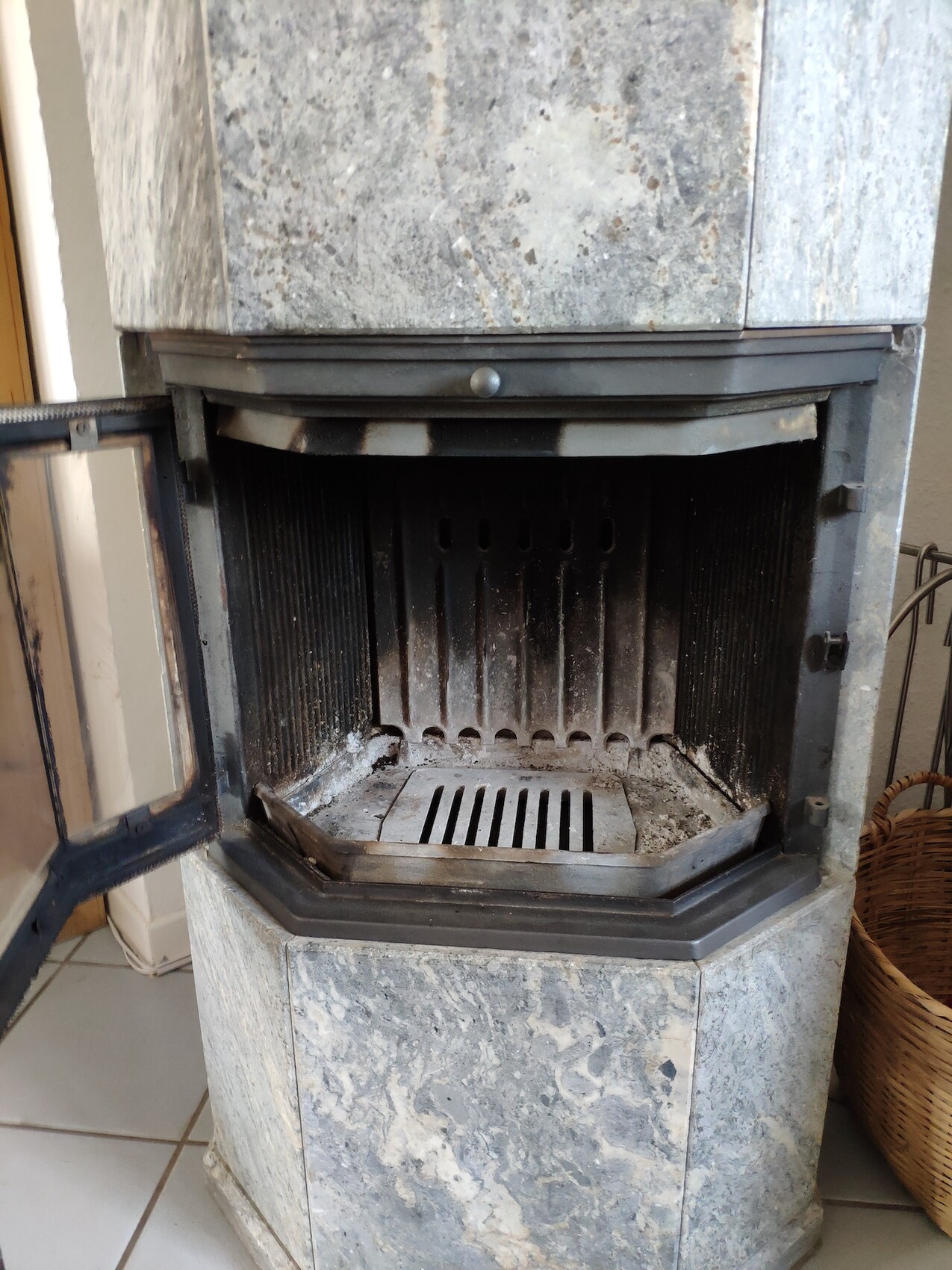 Wood-burning stove made of gray marble with an open door, internal grate, and ash.