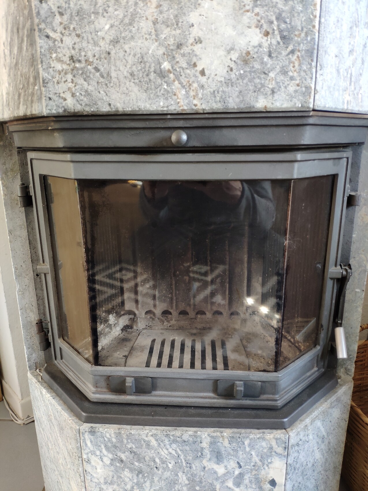 Stone wood-burning stove with glass front and metal frame; interior with grate and ash.