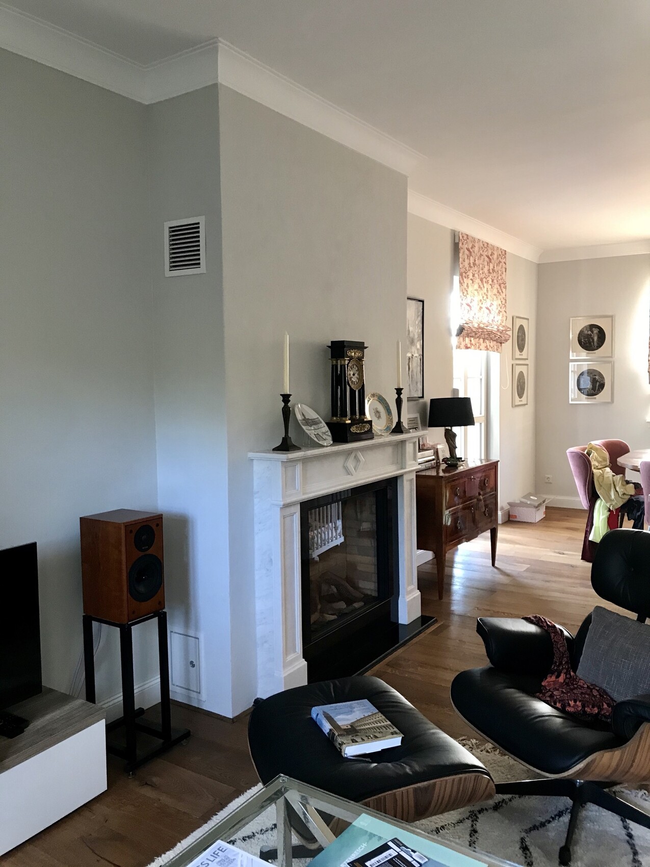 Living room with fireplace, clock on the mantel, candles, leather armchair, coffee table, picture frames on the wall.