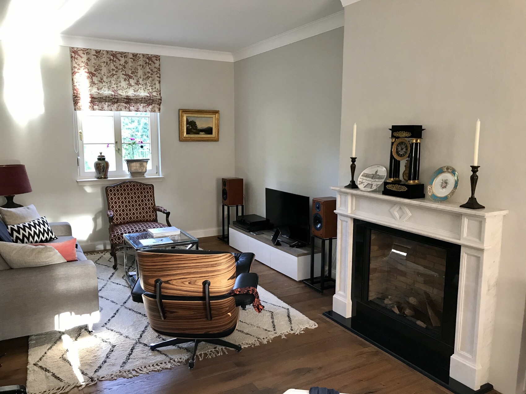 Living room with fireplace, TV area, sofa, armchair and glass coffee table, curtains.