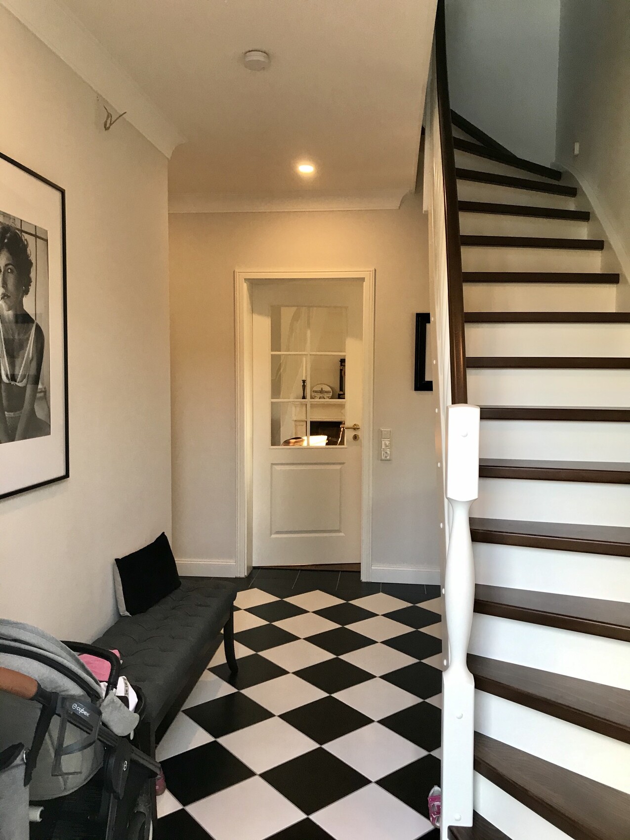 Entrance area with black and white tiles, staircase on the right, bench on the left, door straight ahead.