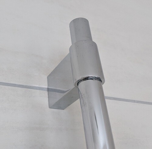 Close-up of a chrome steel pipe with wall bracket on a light wall.