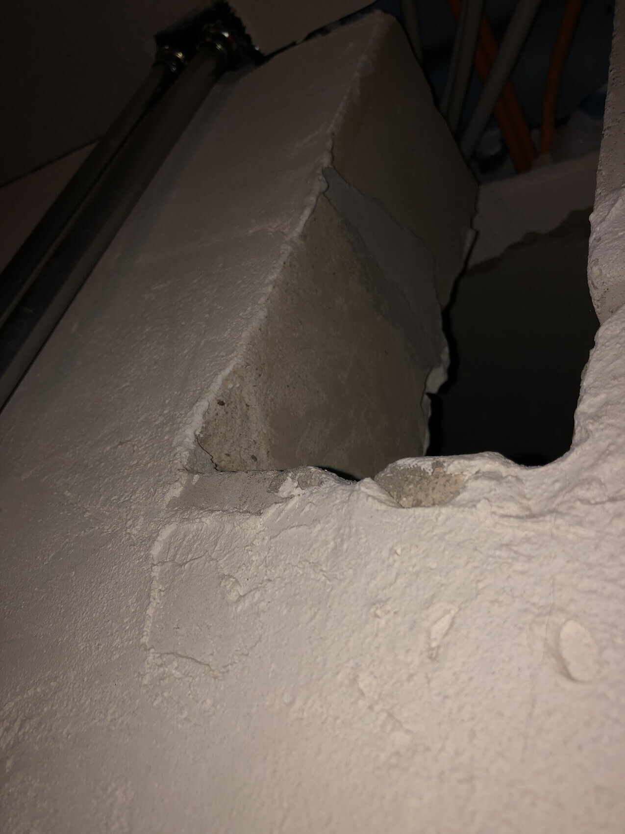 Hole in a rough concrete wall with an open cavity; pipes are visible behind it.