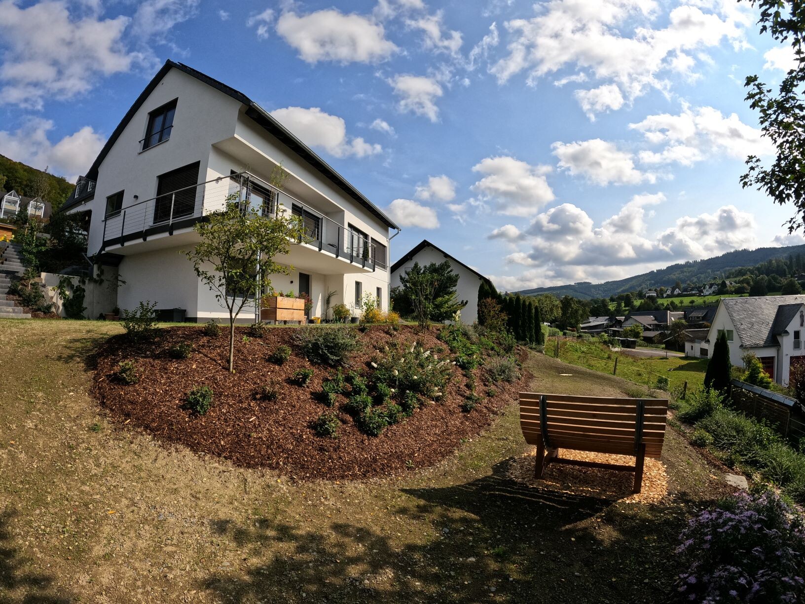 Modern white house facade with garden terrace and bench on sloped plot