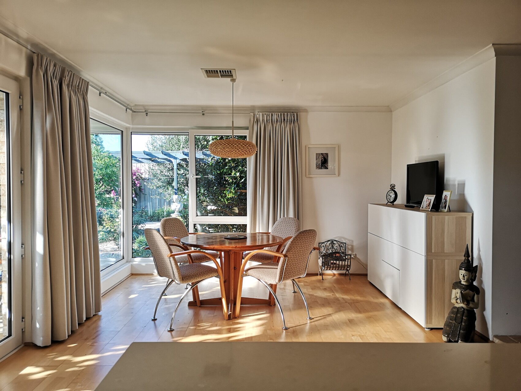 Living room with round wooden table, upholstered chairs, large window front and garden view.
