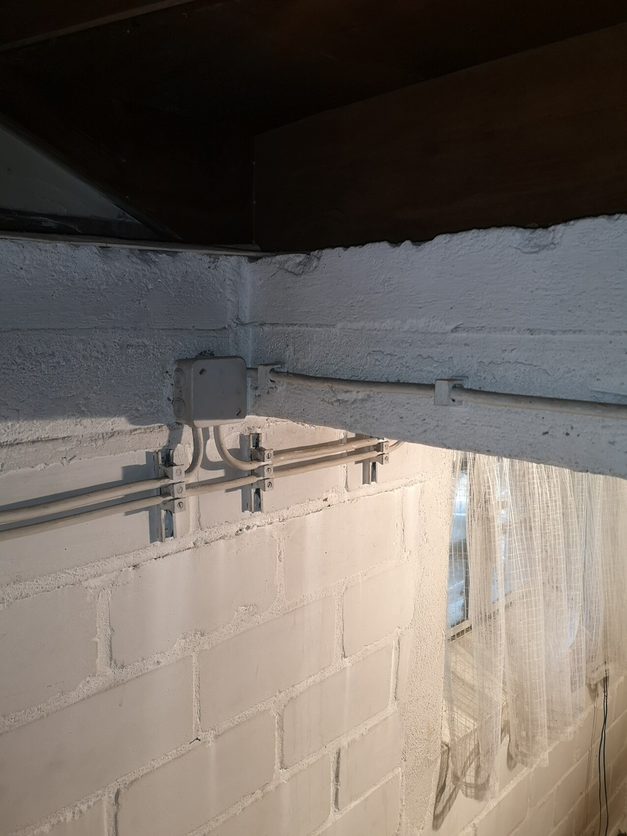 Kellerwand aus Betonblöcken mit grauer Verteilerdose und mehreren Kabelkanälen, Holzbalkendecke