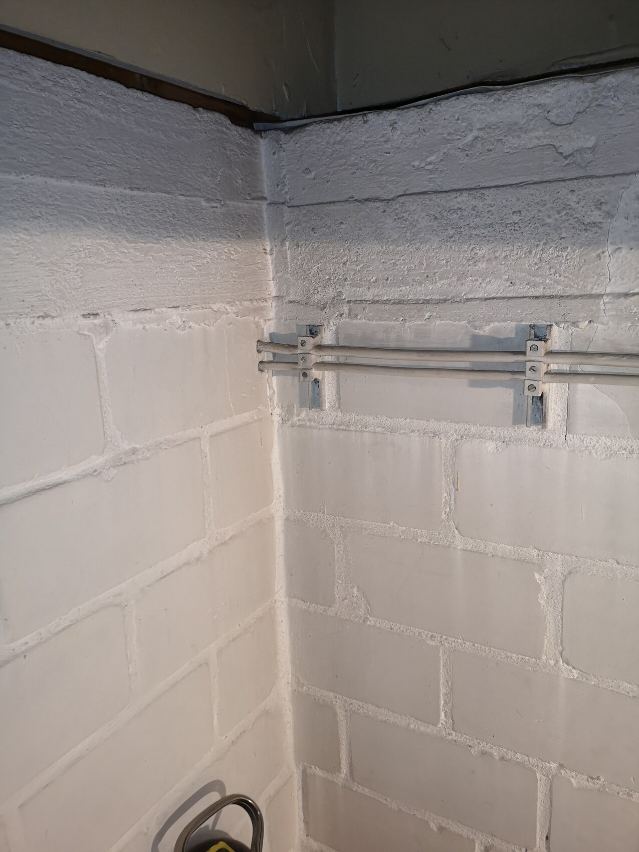 Eckige Kellerwand aus Beton mit zwei parallel verlaufenden Metallrohren an Halterungen.