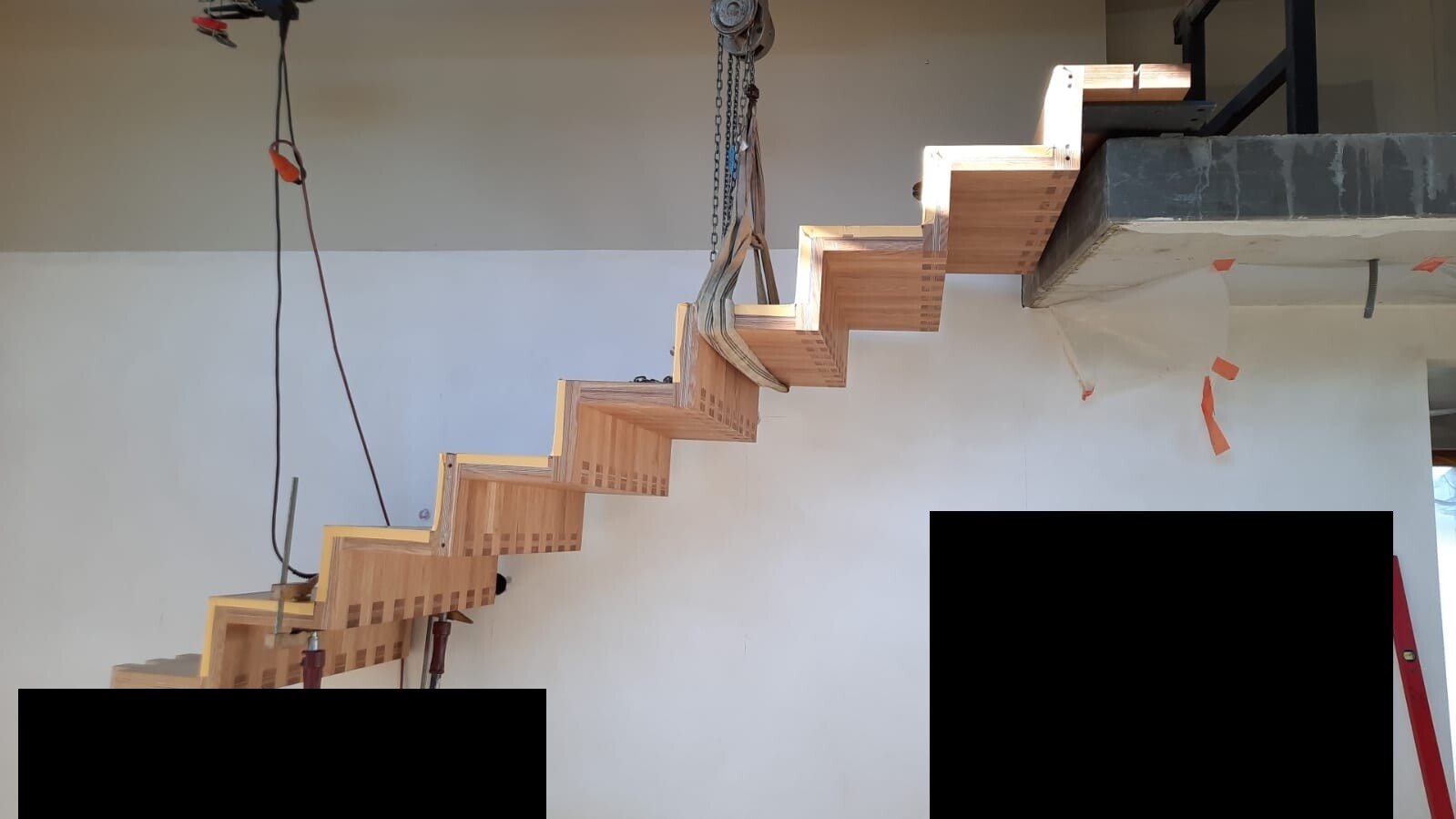 Wooden staircase under construction: angled mounted open steps; crane suspension inside the building.