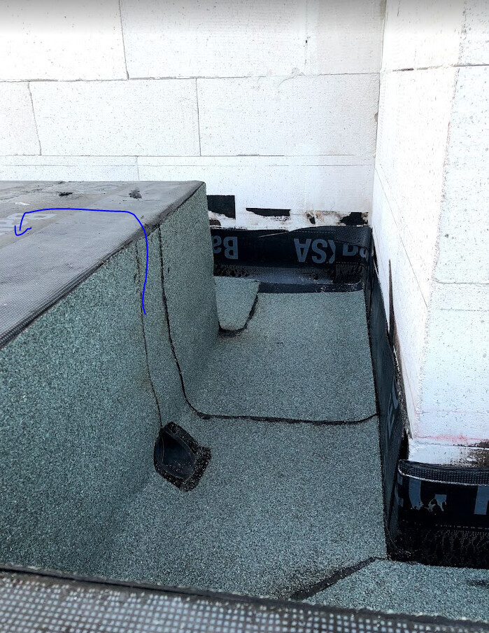 Roof edge with green insulation material, round opening, and black bitumen membrane on white masonry