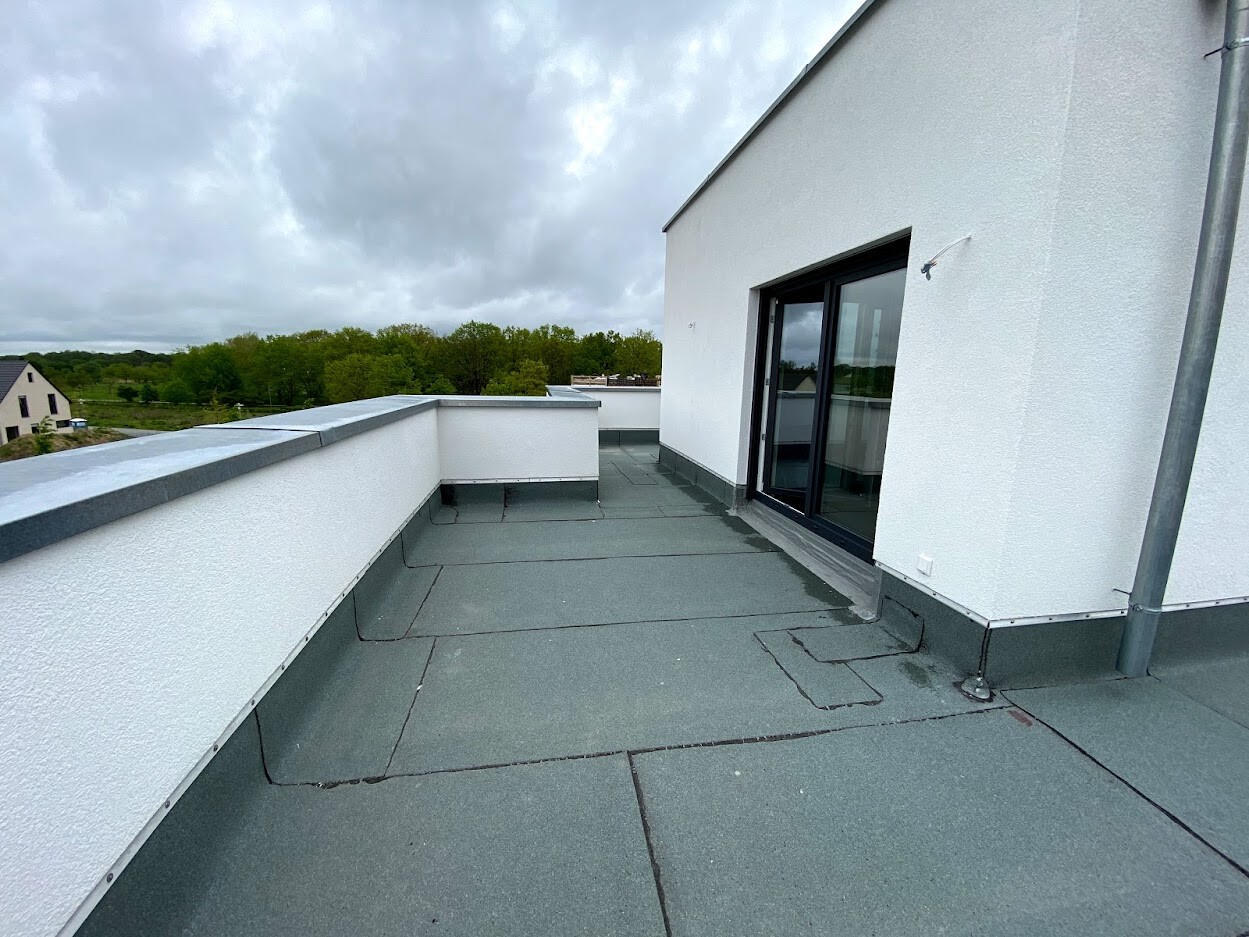 Rooftop terrace of a white building with glass sliding door, gray floor, view of trees