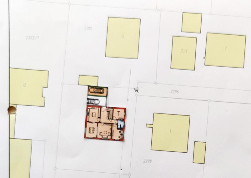 Site plan of a plot with red floor plan and two cars in the garage, surrounding houses.