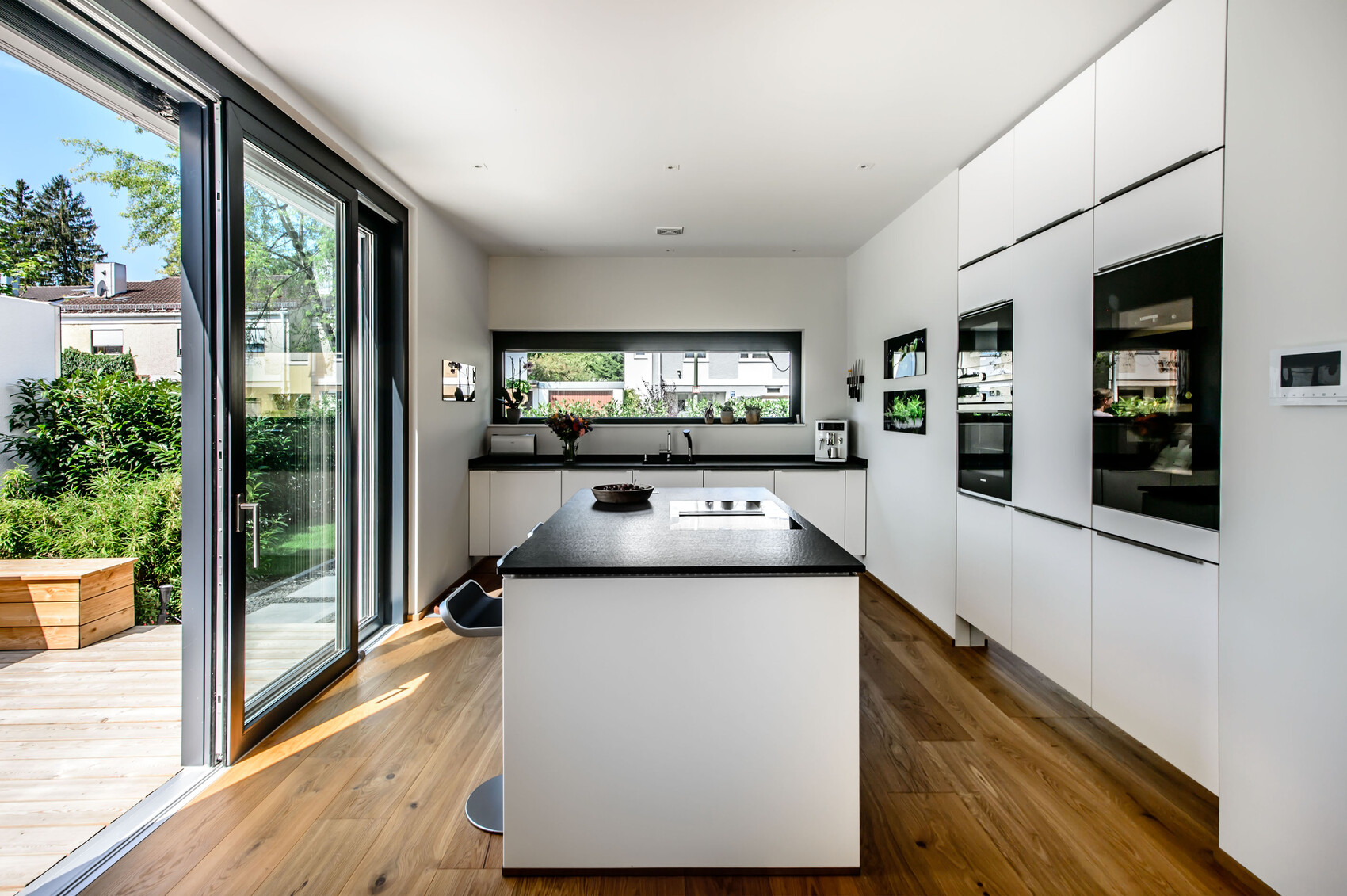 Moderne Kueche mit Insel, weissen Schraenken, schwarzen Arbeitsplatten und Glas-Terrassentueren