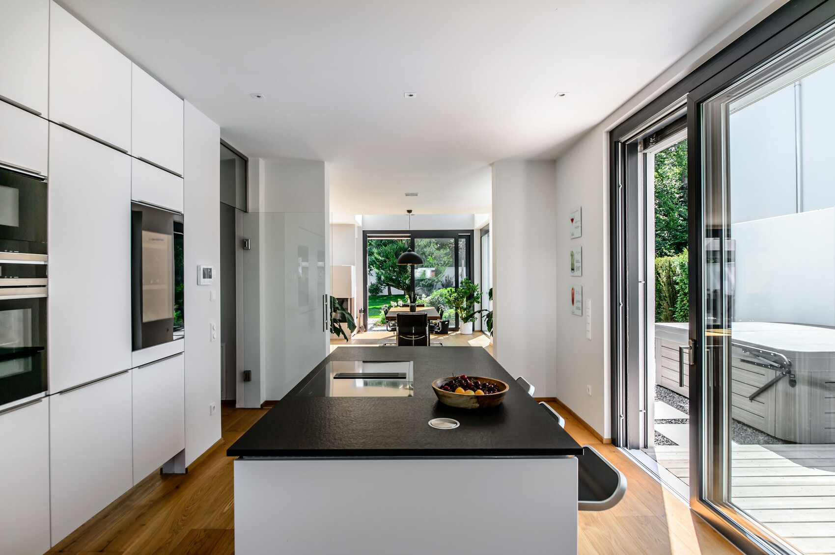 Moderne Küche mit weißen Schränken und dunkler Insel; Blick auf Essbereich und Garten.