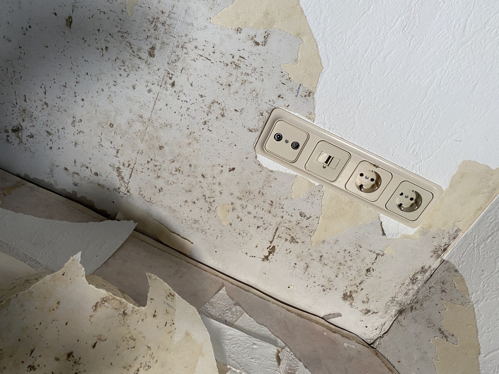 Wall with peeling wallpaper; integrated power strip with USB port and two sockets.