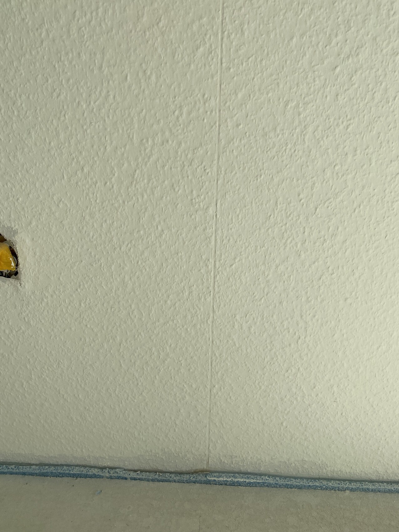 White textured wall with vertical joint; floor covered with blue tape, left opening covered with yellow tape.