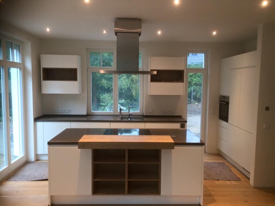 Modern white kitchen with island, wooden countertop, open wine rack, and sink under windows