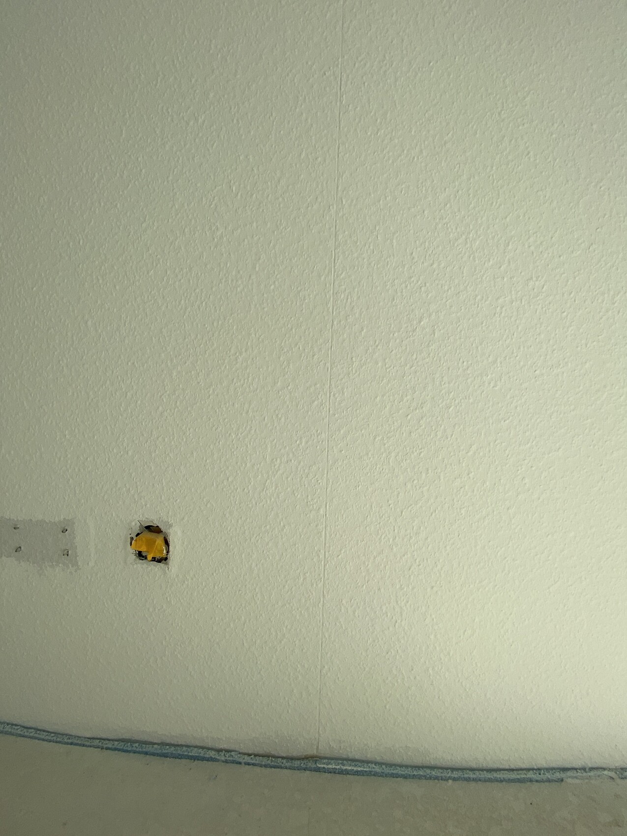 Light wall with small hole and yellow cover near the floor.