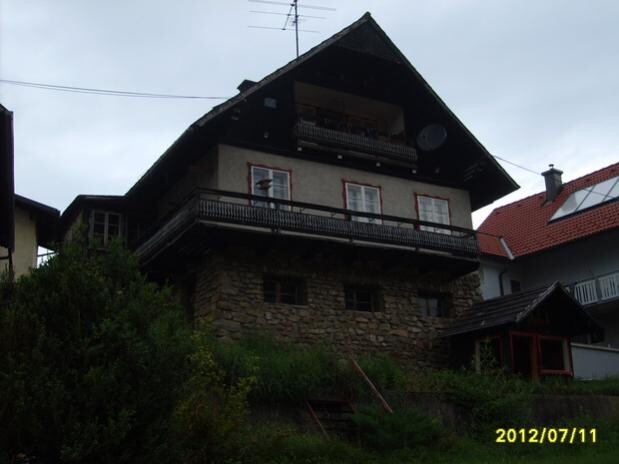 Multi-story house with wooden balustrades, stone foundation and terrace on a slope.