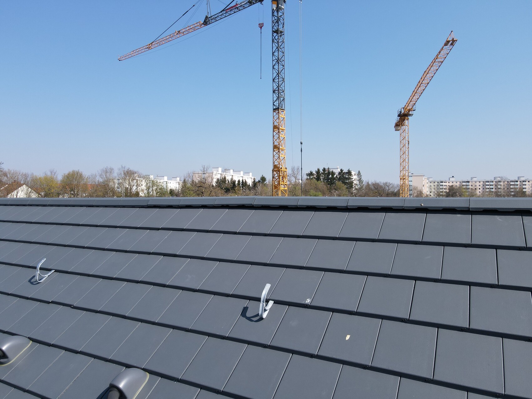 Roof with dark gray tiles, construction cranes in the background at a construction site