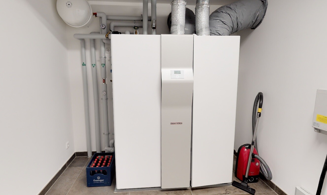 Large heating boiler in a utility room with pipes, pumps, and vacuum cleaner.