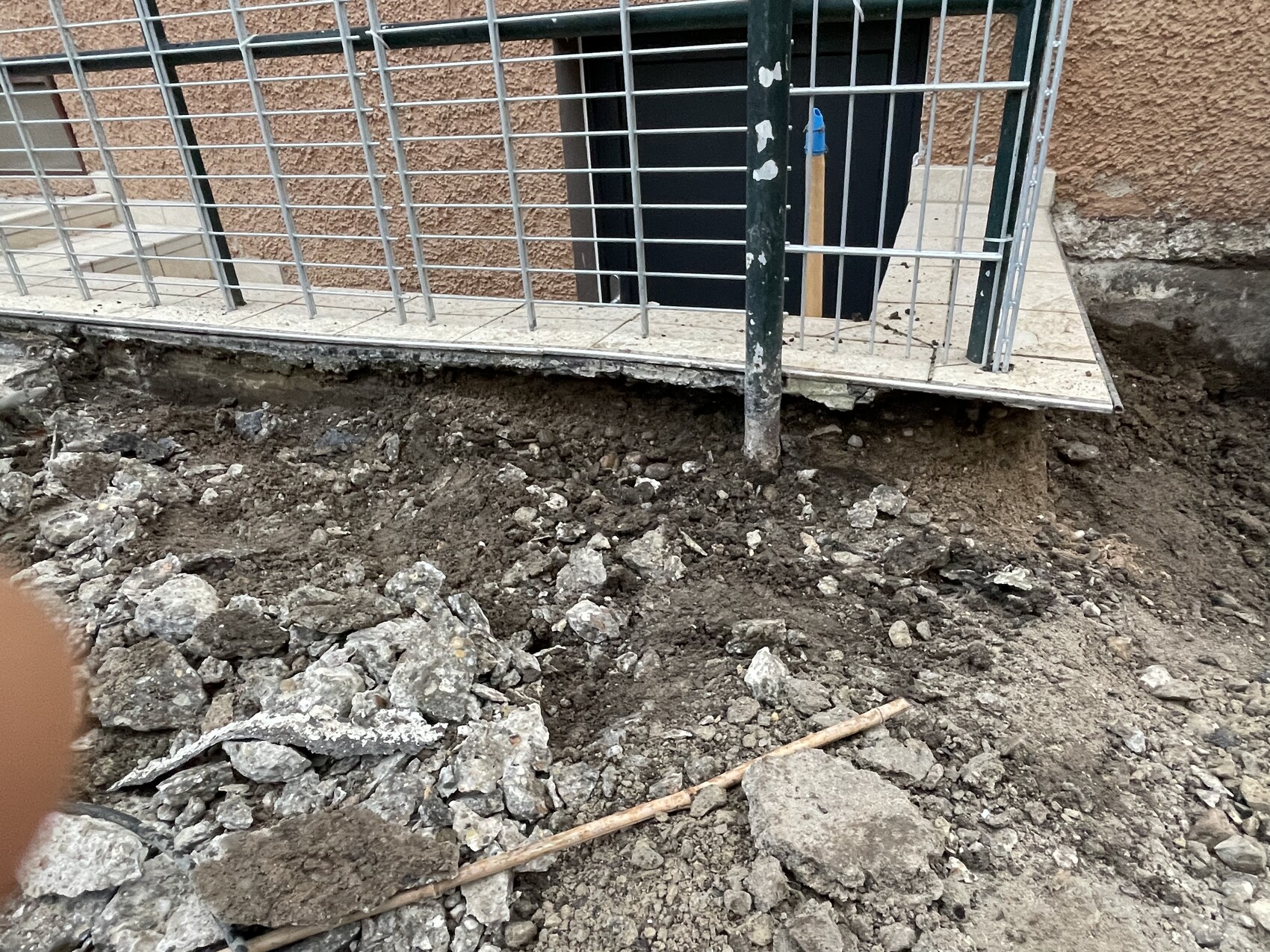 Baugrube mit Erde und Geröll vor einem Metallgitter am Gebäude.