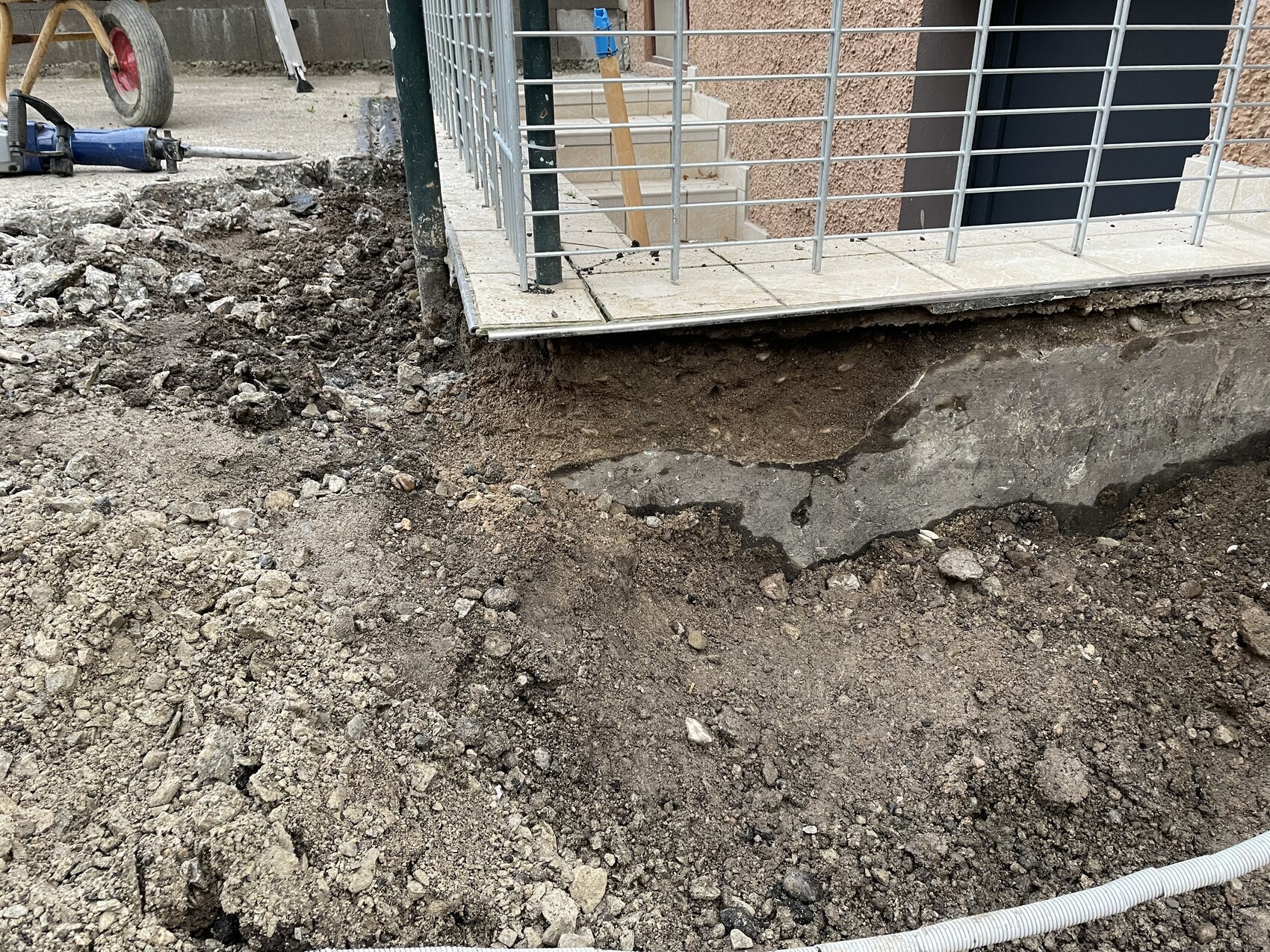 Baugrube am Eingang mit freigelegtem Fundament, Erde und Metallgeländer.