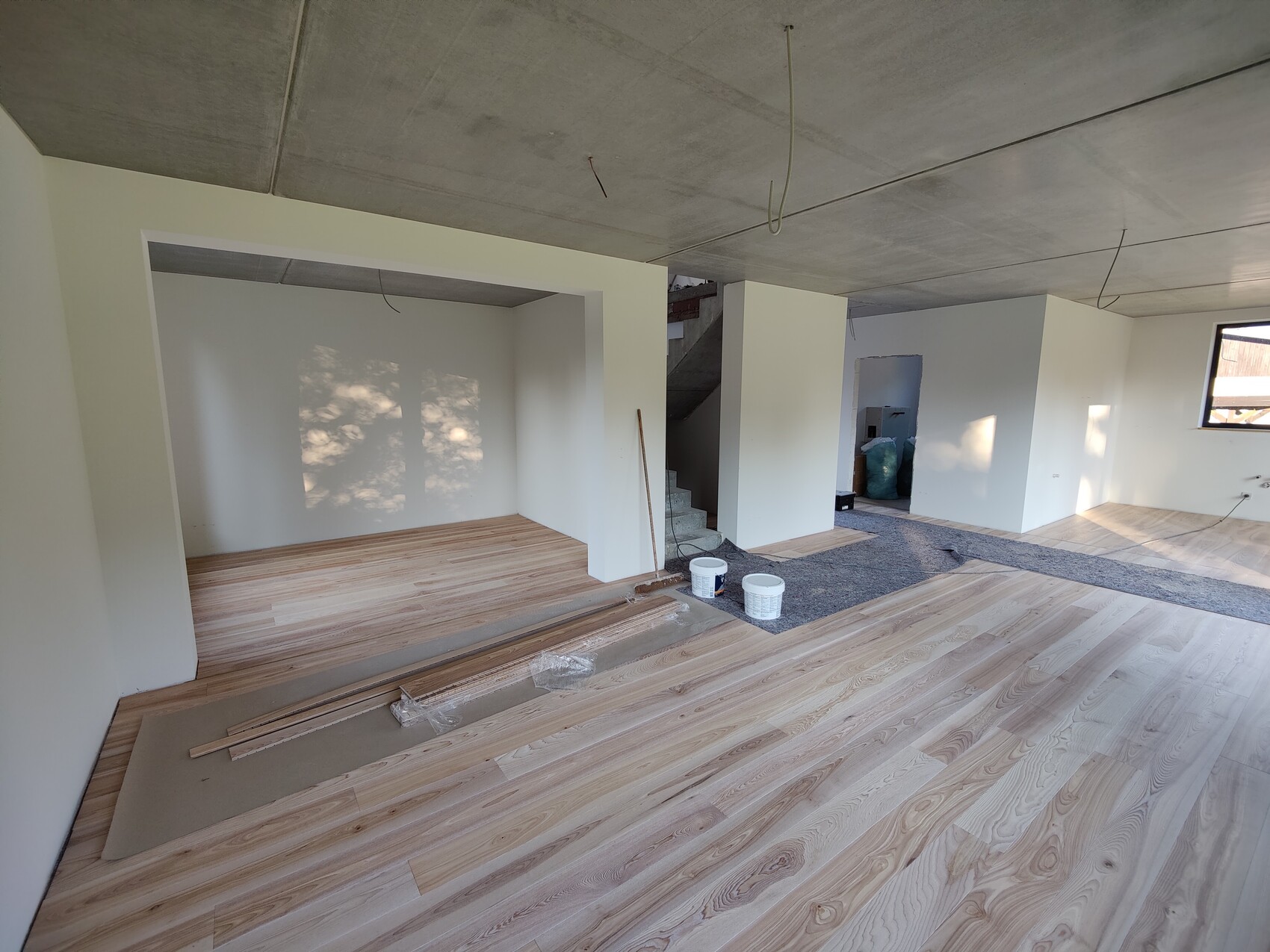 Offenes Renovierungswohnzimmer mit HolzfuĂboden, weiĂen Wänden, Treppe und Baumaterialien.