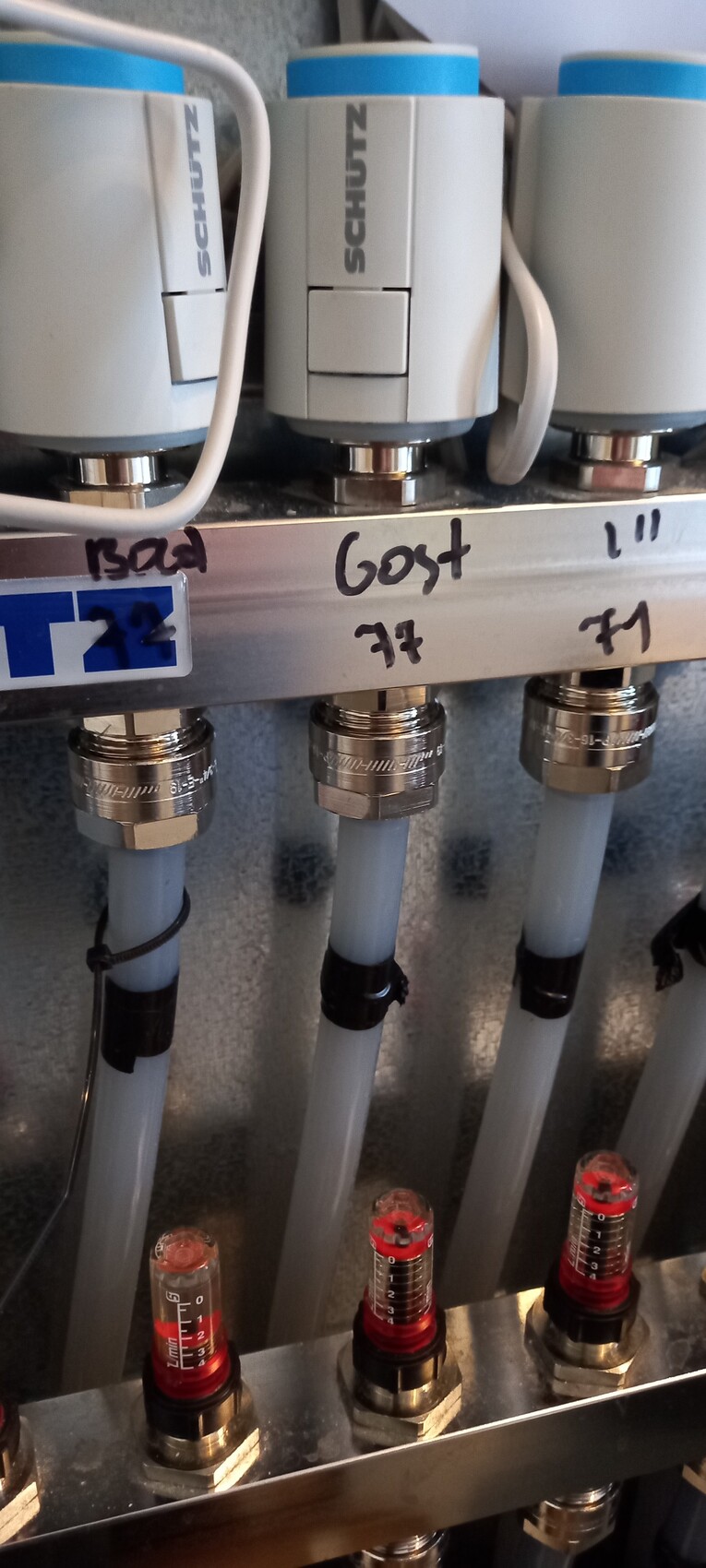 Three gray valves with hoses and pressure gauges on a metal strip.