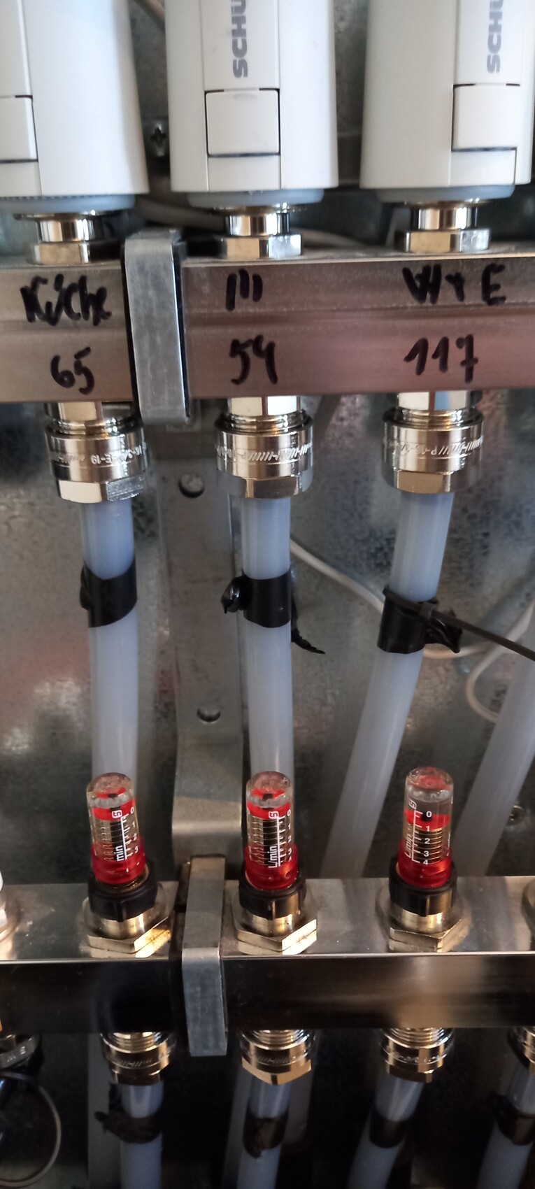 Three vertical glass vessels with red liquid levels in an industrial pipe distribution.