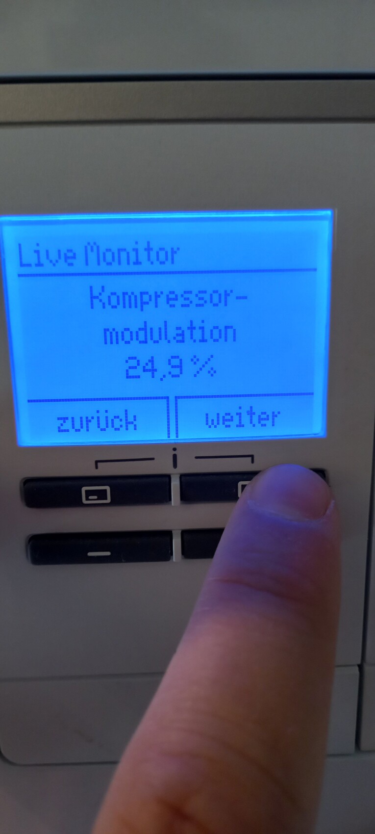 Blaues Display am Bedienfeld zeigt "Live Monitor" und "Kompressor-modulation 24,9%"; Finger drückt Knopf.