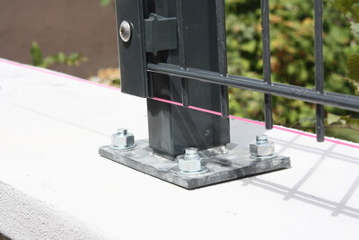 Metal base plate secured fence post to concrete with anchor bolts.