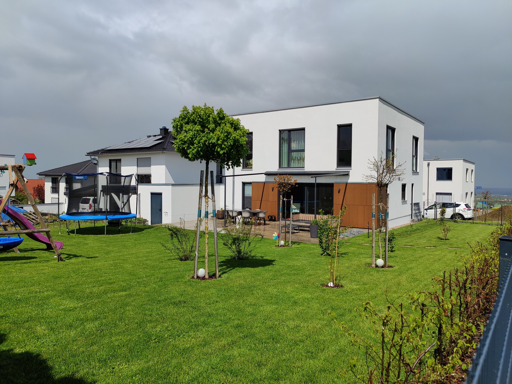 Modern white residential building with terrace, large garden and trampoline play area.