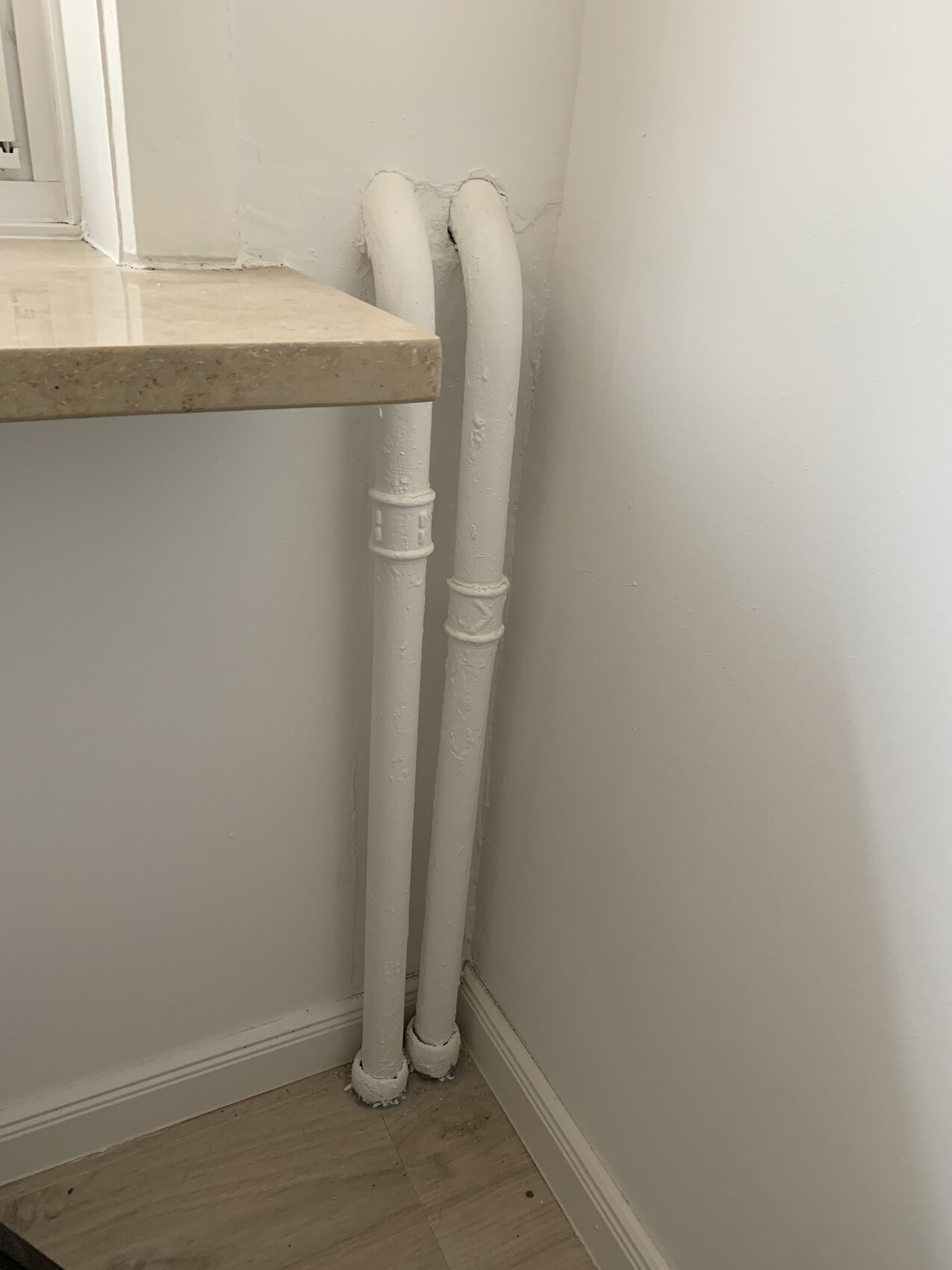 Two white pipes run vertically along the wall next to the kitchen counter, fixed at the floor.
