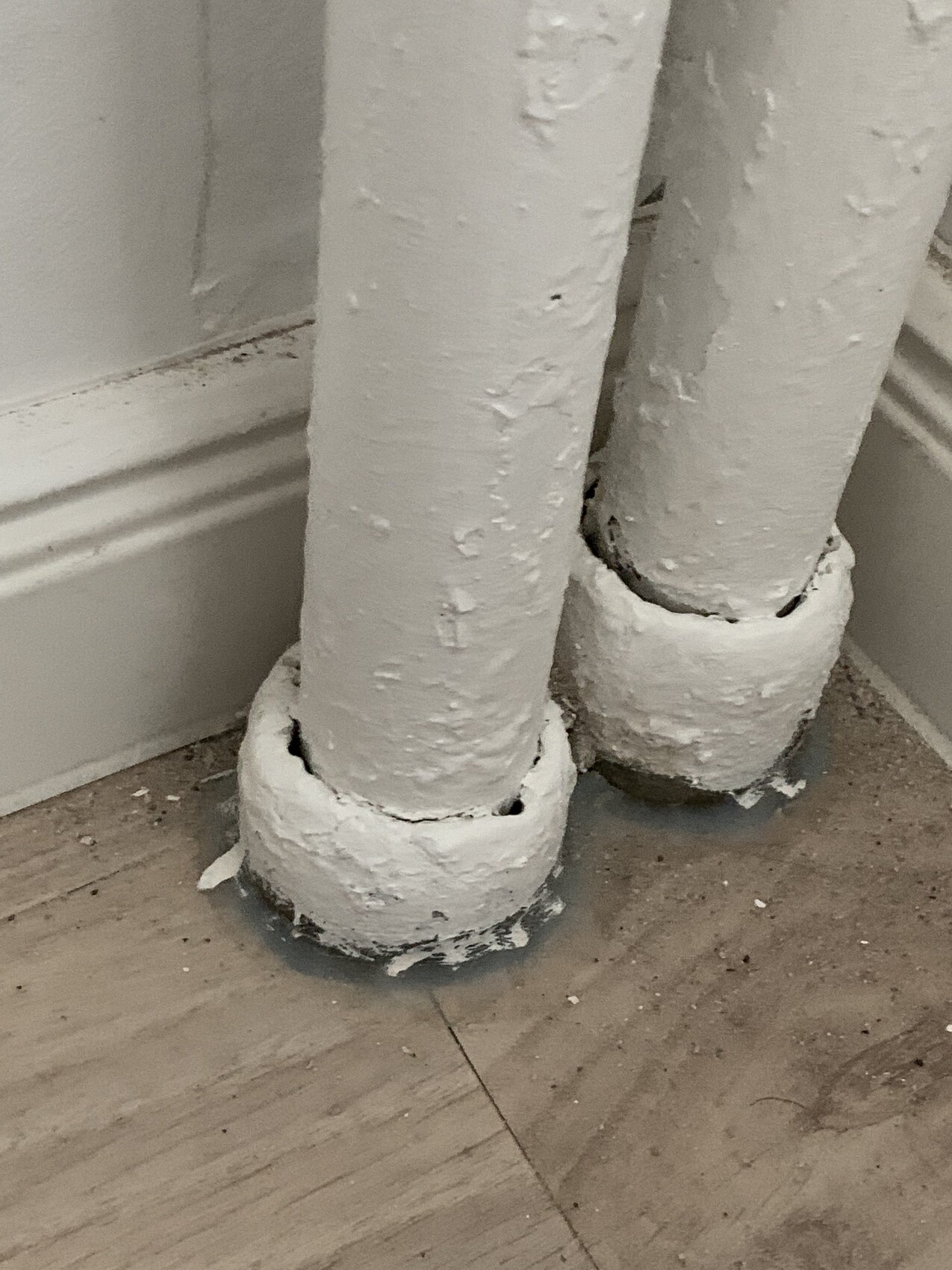 Two white pipes with chipped paint stand close to a wall on a wooden floor.