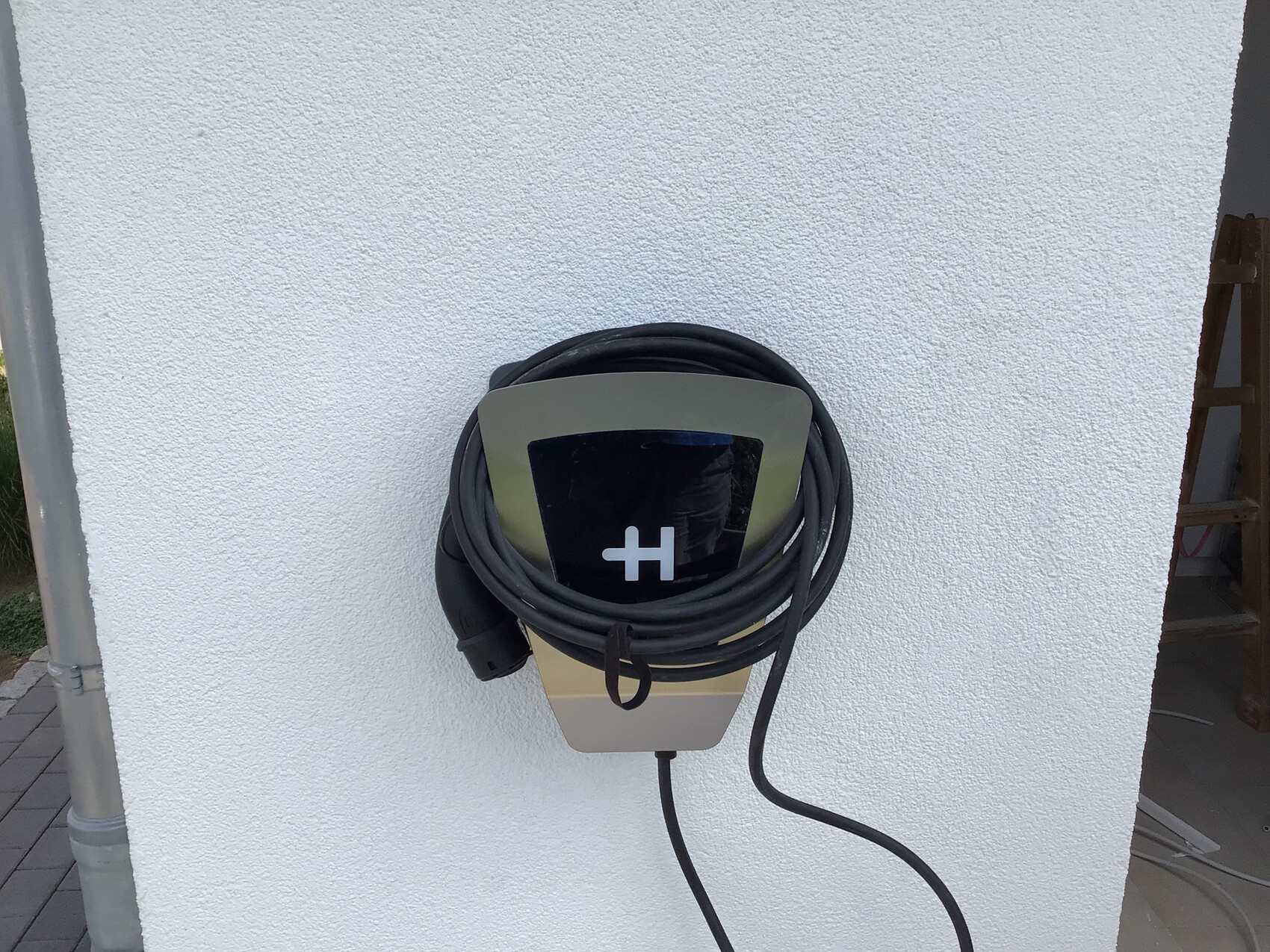 Wall-mounted electric car charging station with coiled cable in front of white plaster wall
